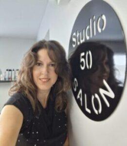 Interior view of Studio 50 Salon with a smiling stylist in front of the salon logo.